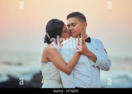 Portrait of Hispanic couple kissing sunset floue sur fond orange. L'époux et épouse kiss Banque D'Images