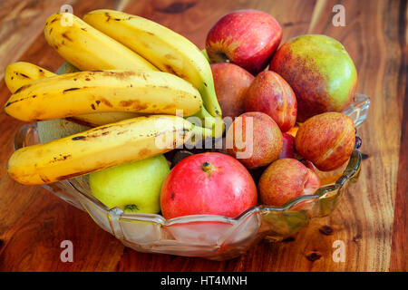 Un bol de fruits en verre avec une variété de produits frais, sains et nutricious composé de fruits bananes, pommes, prunes et mangue Banque D'Images