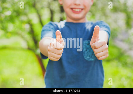 Handsome cheerful 9 ans garçon montrant deux mains avec les pouces jusqu'en appareil photo comme symbole de réussite. Close up of fingers avec accent sur eux et trouble Banque D'Images