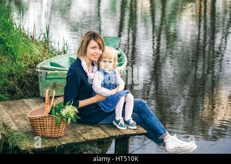 Portrait de famille heureuse de deux personnes en vacances. Jeune mère et fille on picnic près de spring river et vieux bateau en bois plus belle wa Banque D'Images