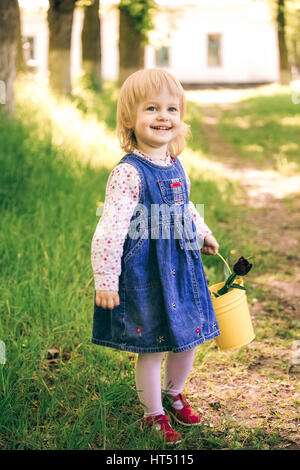 Portrait of happy little girl blonde avec godet jaune fleurs tulipes. Cute funny enfant se trouve dans le jardin de printemps ensoleillé dans la campagne. Moins de ch Banque D'Images