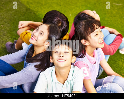 De l'école élémentaire du groupe asiatique filles et garçons assis sur l'herbe à aire le ciel Banque D'Images