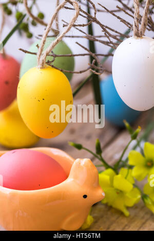 La composition avec décoration de Pâques oeufs hanging on branch, jaune fleurs de printemps, tasse de porcelaine en forme de bois de grange de poulet style rustique, l'arrière-plan Banque D'Images