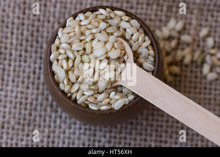 Riz brun à grains entiers dans un bol avec une cuillère de bois de feu, sur de la toile de jute, tissu top view, Close up, style rustique Banque D'Images