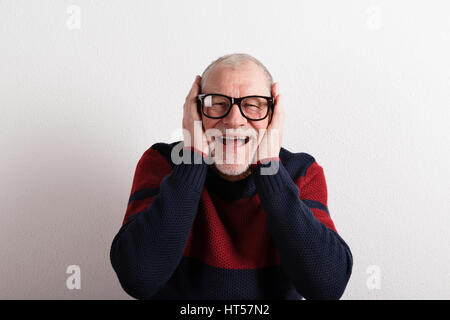 Happy senior man in red et pull bleu et noir lunettes tenant tête. Studio shot contre le mur blanc. Banque D'Images