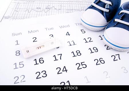 Test de grossesse positif sur le calendrier et les chaussons bébé Banque D'Images