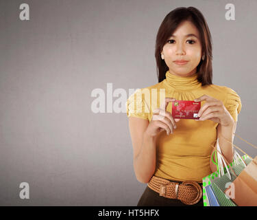 Happy asian woman avec de nombreux sacs de shopping et une carte de crédit dans sa main contre l'arrière-plan gris Banque D'Images