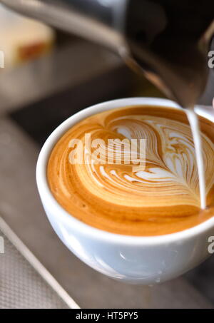 Café en tasse avec de belles tourbillonner sur le dessus, avec un croissant sur le côté, sur la table. Banque D'Images