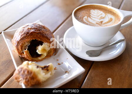 Café en tasse avec de belles tourbillonner sur le dessus, avec un croissant sur le côté, sur la table. Banque D'Images