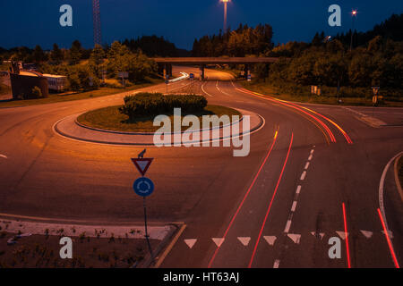 Carrefour/rond-point, au crépuscule, avec des pistes de voitures. Banque D'Images