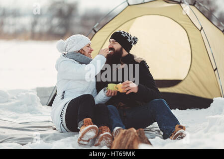 Couple heureux dans des vêtements chauds sont assis dans la neige sur le fond de la tente les amateurs de tourisme, de rire et de profiter du repos et de la nature enneigée Banque D'Images