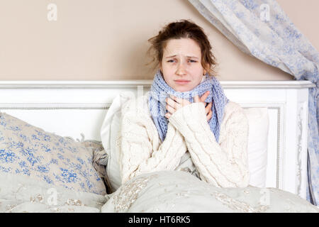 Femme malade avec de terribles maux de gorge. Libre de droit de jeune femme avec nez rouge au lit avec foulard épais et de toucher son cou et de la tête la sensation de douleur Banque D'Images