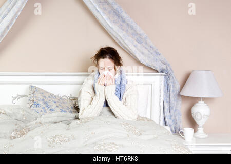 Femme malade avec de terribles maux de gorge. Libre de droit de jeune femme avec nez rouge au lit avec foulard épais et de toucher son cou et de la tête la sensation de douleur Banque D'Images