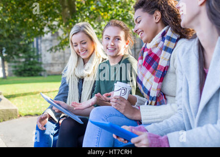 Quatre heureux filles rire et sourire ensemble comme ils jouissent de l'étude de l'extérieur. Ils s'intéressent aux tablettes numériques dans leurs mains. Banque D'Images