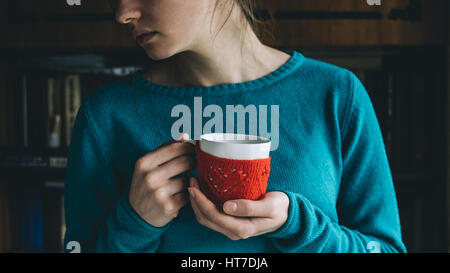 Jeune femme de couleur menthe en buvant un café chaud, pull en tricot rouge Mug de moufle. Emmitouflés, obtenez chaud concept Banque D'Images
