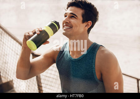 Close up shot of young man drinking water après entraînement à l'extérieur. Coureur mâle se reposant après une séance de formation et de rire. Banque D'Images