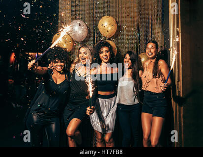 Photo de groupe de jeunes femmes célébrant le nouvel an au pub. Groupe d'amis féminins avec baguettes à la fête dans une discothèque. Banque D'Images