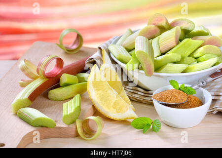 Pelé et haché matières rhubarbe compote préparés pour la cuisson avec du sucre brun et de citron, à l'arrière-plan d'autres tiges de rhubarbe dans soft focus Banque D'Images
