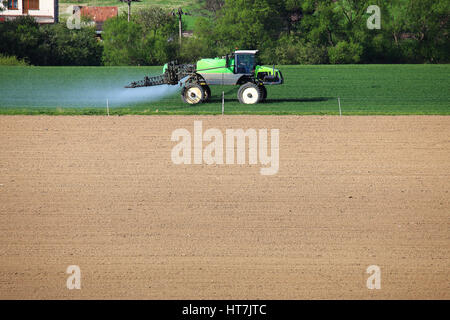 Tracteur vert sur champ. Champ de blé vert féconde du tracteur. Spraing du tracteur de l'eau sur les cultures. Espace libre pour le texte sur fond de sol brun. Printemps agr Banque D'Images