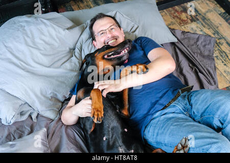 L'homme au lit avec big black dog doberman Banque D'Images