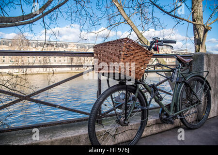Un vélo vintage avec un panier en osier s'appuie contre une rambarde sur les rives de la Seine à Paris France. Banque D'Images