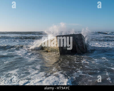 Bunker en béton sur la plage comme la pulvérisation d'eau par les vagues. Le bunker est à moitié enfoncé dans le fond marin Banque D'Images