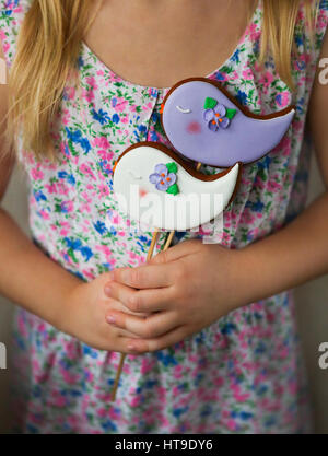 Little girl holding violet et blanc cookies avec les oiseaux dans ses mains Banque D'Images