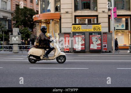 Une personne montant un moto scooter Vespa beige dans la ville de Madrid (Espagne) en 2017. Banque D'Images