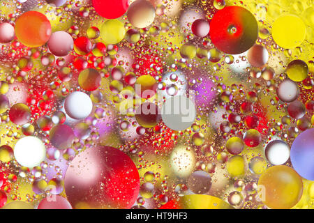 Gouttes d'huile rétroéclairé flottant dans l'eau sur de perles de couleur Banque D'Images