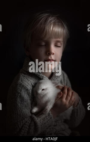 Un petit garçon tenant un lapin blanc et fermer les yeux Banque D'Images