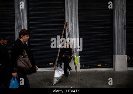 Un homme vend des billets de loterie qu'il siège à l'extérieur d'un atelier fermé à Athènes le 7 mars 2017. Photo : Angelos Tzortzinis/dpa Banque D'Images