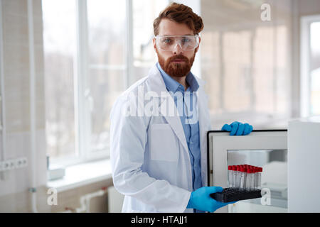 Clinicien sérieux mettant flacons avec des échantillons de laboratoire de stockage dans un coffre-fort Banque D'Images