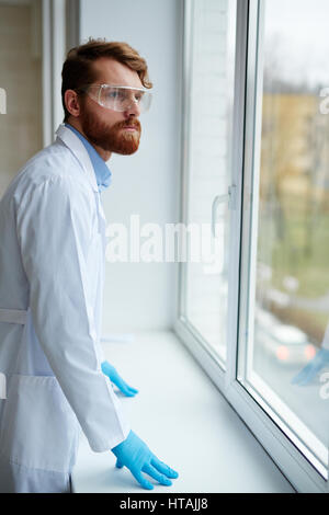Jeune homme sérieux en uniforme à la fenêtre en laboratoire Banque D'Images