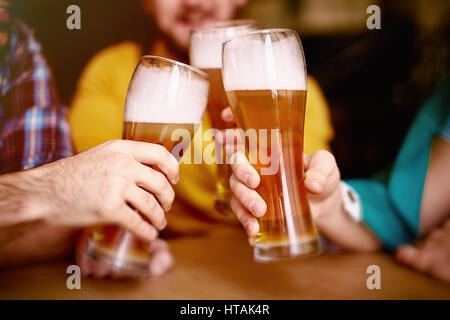 Libre tourné de trois élégantes des grands verres à bière blonde artisanale délicieux et haut en mousse visco mains des hommes séance table ronde à Irish Pub Banque D'Images