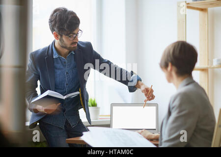 Aider les jeunes femmes élégantes manager collègue des problèmes liés au travail en pointant sur l'écran du portable en blanc et l'explication des plans dans un bureau moderne Banque D'Images
