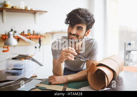 Portrait of handsome middle eastern woman coupe de cheveux créatif à l'écart et souriant, penché sur la table de l'atelier lors de la création de dessins et modèles industriels en cuir Banque D'Images