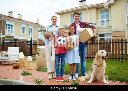 Portrait de famille heureuse avec deux enfants et leur chien golden retriever debout à l'extérieur tenant des boîtes de carton et d'effets personnels à l'avant o Banque D'Images