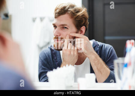 Jeune homme presser bouton sur sa joue en face du miroir Banque D'Images