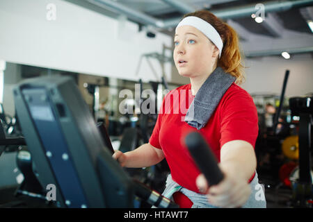 Portrait of cute surpoids femme aux cheveux rouges l'utilisation de machines de fitness pour perdre du poids Banque D'Images