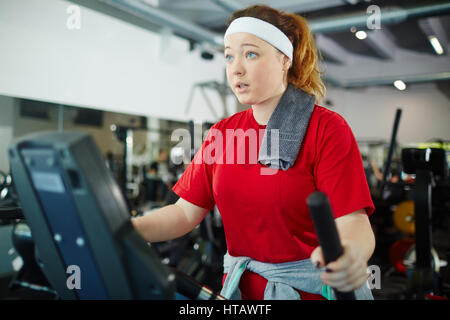 Surpoids cute girl with red hair travaillant à l'aide de machines dans une salle de sport, de rêver à être plus mince Banque D'Images