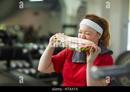 Portrait of young woman eating surpoids gros sandwich engraissement prendre une pause pour s'entraîner dans la salle de sport, concept de l'obsession alimentaire Banque D'Images