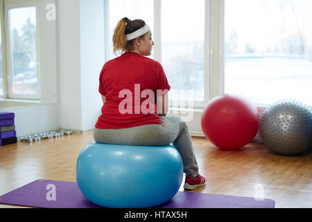 Vue arrière de l'excès de portrait woman working out in fitness studio : rebondir sur big fitness ball looking away Banque D'Images