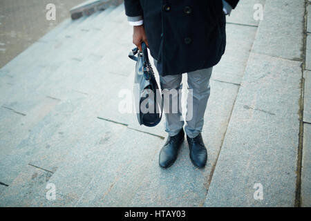 Portrait de l'un de l'article faible méconnaissable businessman standing on steps of office building portant manteau, chaussures en cuir brillant et holding briefcase Banque D'Images
