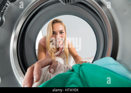 Young Smiling Woman Chargement à l'intérieur de la machine à laver Banque D'Images