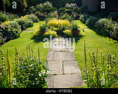 Chenies Manor jardin en contrebas en fin d'après-midi avec la lumière du soleil et d'ombre autour de l'étang ornemental, encadrée par les plantes et fleurs de la frontière de hauteur. Banque D'Images