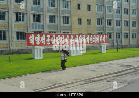 09.08.2012, Pyongyang, Corée du Nord - une femme est vu marchant à côté d'une rue dans le centre de Pyongyang avec bâtiments résidentiels à la toile. Banque D'Images