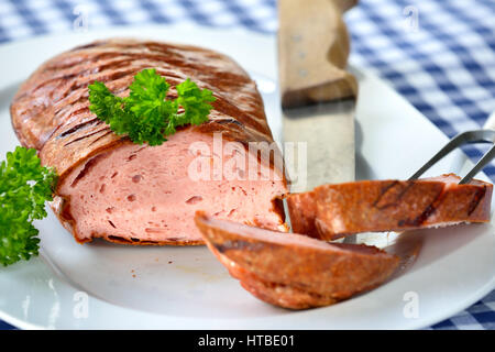 Pain de viande bavarois sur une assiette blanche servi sur une table avec une nappe à carreaux bleu et blanc Banque D'Images