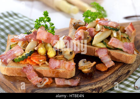 Pain grillé avec des asperges blanches, d'autres légumes et bacon, servi sur une planche en bois Banque D'Images