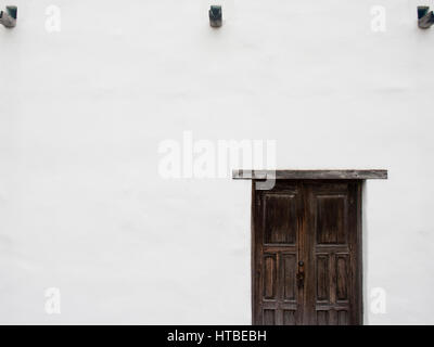 Une porte en bois brun foncé rustique se détache sur le mur blanc d'un bâtiment d'adobe. Banque D'Images