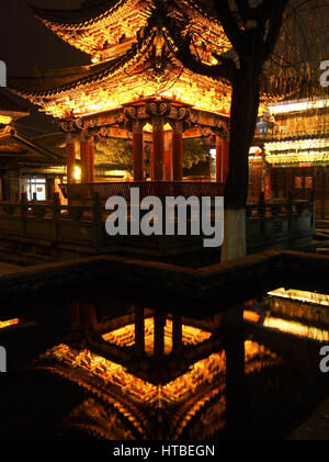 Une pagode est éclairé la nuit à Dali, Chine avec la structure traditionnelle reflète dans petit étang. Banque D'Images